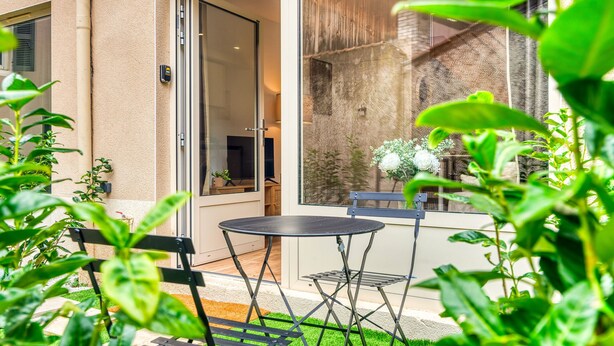 Un patio con mesa y sillas, una puerta corrediza de vidrio y vistas a una cerca de madera y árboles.