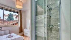 Un dormitorio moderno con un ventanal grande, cabina de ducha de vidrio y cama bien hecha.