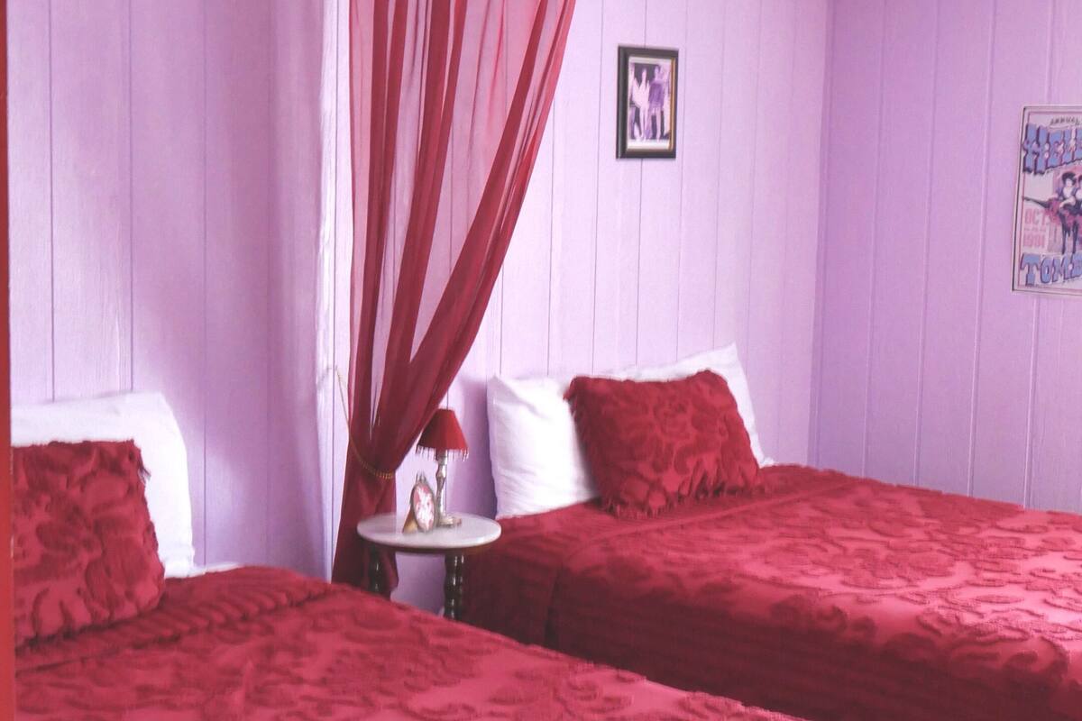 A room with two beds, a ceiling fan, a small table with a lamp, and a poster on the wall.