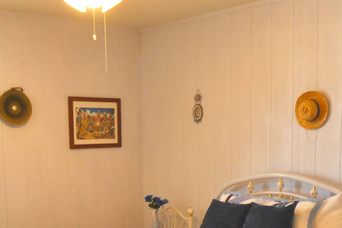 A neatly made bed with a patterned bedspread, a bedside table with a vase of flowers, and a ceiling fan.