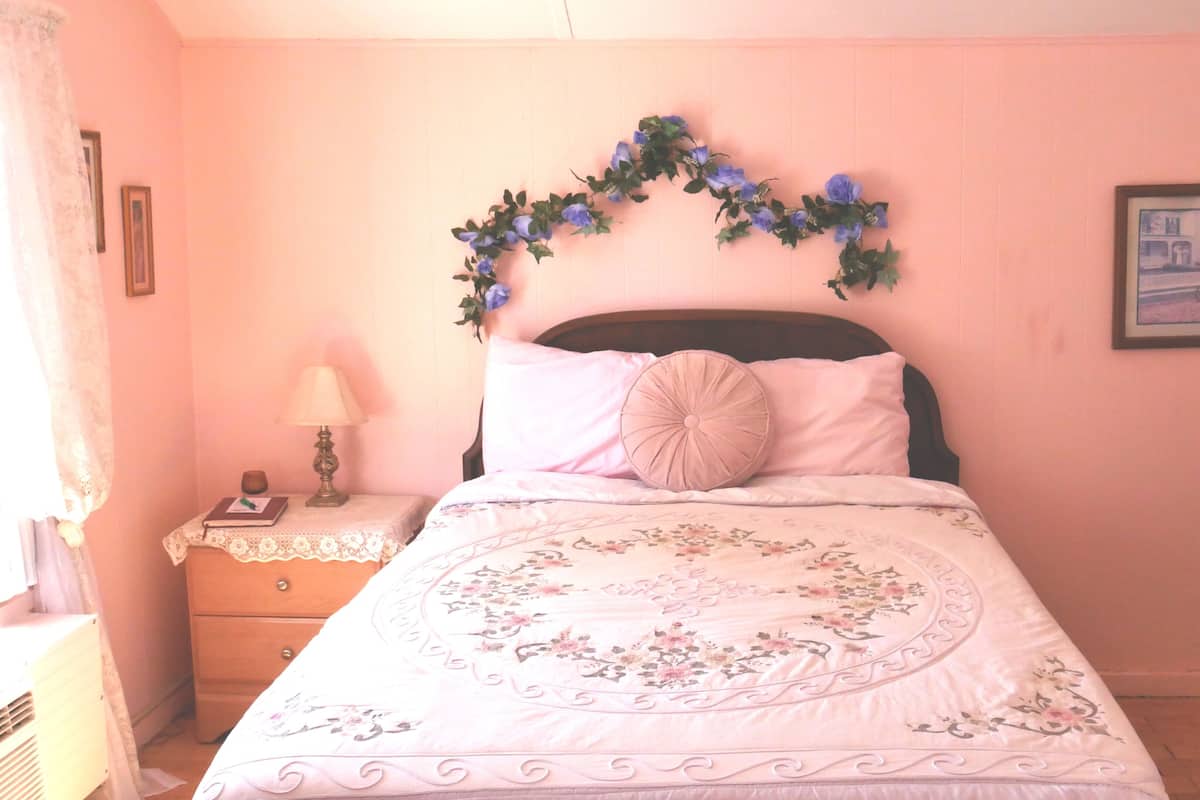 A bedroom with a bed, a nightstand, a lamp, a framed picture on the wall, and a floral headboard.