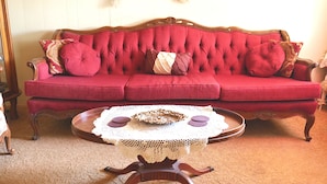 A red upholstered sofa with a decorative backrest, a wooden coffee table with a lace table runner, and a small round table with a white lace table runner. - The Tombstone Bordello  (Tombstone)