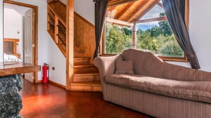 Una escalera de madera conduce a una habitación superior con un gran ventanal que ofrece vistas a árboles.