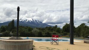 Zona de piscina con terraza de madera, una silla roja y una montaña al fondo.