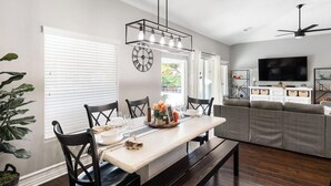 A modern living room with a grey sofa, a flat-screen TV, and a dining area with a wooden table and chairs. - Heated Pool at Turtle Cove Sleeps 12 (Mesquite)