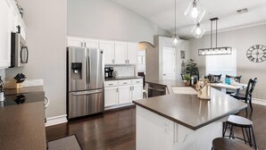 A modern kitchen with stainless steel appliances, a central island, pendant lighting, and a dining area with a clock on the wall. - Heated Pool at Turtle Cove Sleeps 12 (Mesquite)