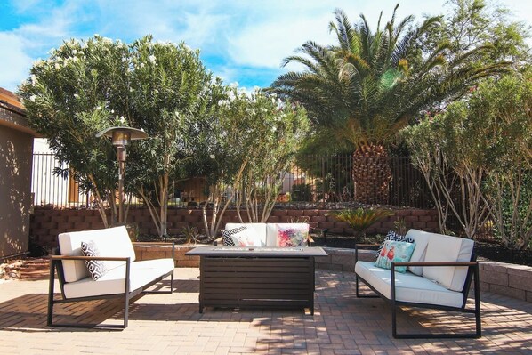 An outdoor patio with a wooden table and two white sofas with patterned cushions.