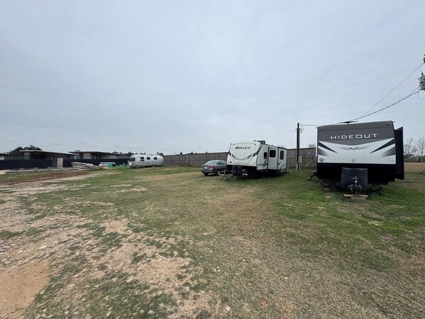 A campsite with RVs and trailers, including a 'Hideout' and a 'Bullet' model, in a grassy area with buildings in the background.