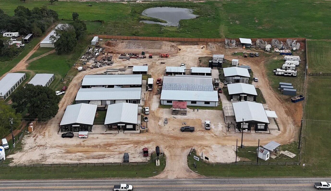 An industrial area with multiple buildings, a dirt road, and a fenced perimeter.