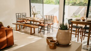 Un comedor moderno con mesas y bancos de madera, un ventanal con vistas al exterior y una planta en maceta sobre una mesa.