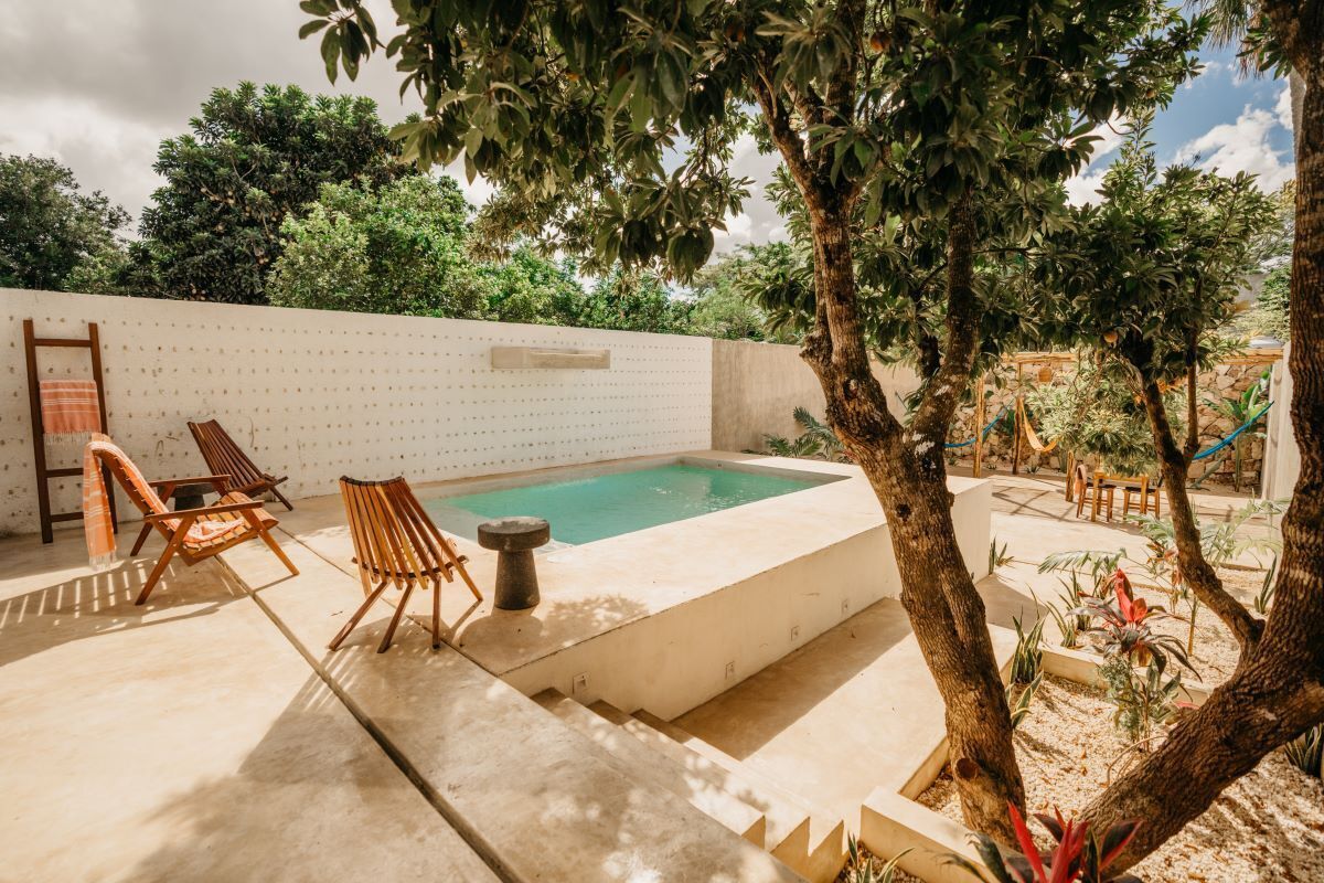 A pool area with a white wall, two wooden chairs, and a small table.