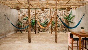 Un espacio al aire libre con mesa y sillas de madera, un muro de piedra y una hamaca colgante.