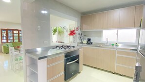 A modern kitchen with a gas stove, oven, and a sink. There is a dining area with a green sofa and white chairs. - Private house with pool - Riohacha, La Guajira. Colombia (Riohacha)