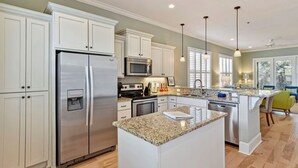 A modern kitchen with white cabinetry, stainless steel appliances, granite countertops, and pendant lighting.