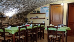 C’est un restaurant aux murs de pierre, aux tables et aux chaises en bois. On y trouve des bouteilles de vin sur des étagères et un menu affiché au mur.