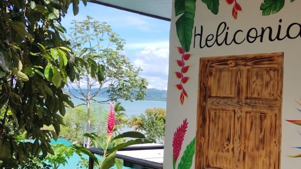 A room with a wooden door, a view of the outdoors, and a wall with tropical plant illustrations. - Ecolodge Kala Luna Resort (Drake Bay)