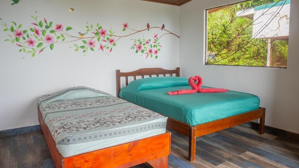 A room with two wooden beds, one with a floral bedspread and the other with a teal bedspread and a red flamingo decoration.