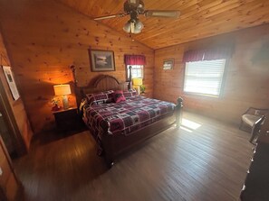 Ein Schlafzimmer einer Holzhütte mit Bett, Deckenventilator und Fenster mit Jalousien.