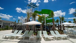 A pool area with lounge chairs, a water slide, and a lifeguard tower. - Windsor Cay 5BR Villa | Private Pool & Game Loft (Clermont)