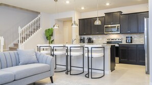A modern kitchen with dark cabinets, a stainless steel refrigerator, and a central island with bar stools. - Windsor Cay 5BR Villa | Private Pool & Game Loft (Clermont)
