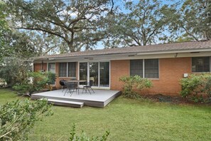 A single-story house with a covered patio, a brick exterior, and a lawn. - Lanier Cottage - cozy home within walking distance to the beach (Jekyll Island)
