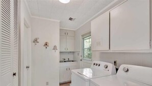 Un cuarto de lavandería con lavadora, secadora y una pequeña zona de kitchenette con pileta y alacenas.