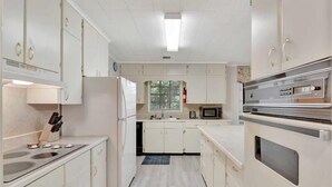 Una cocina estrecha con armarios blancos, un microondas, una estufa y un refrigerador.