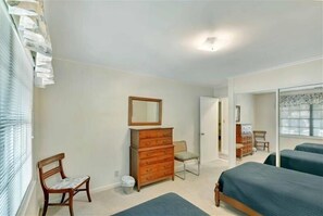 A bedroom with a wooden dresser, a chair, a bed, and a window with blinds. - Lanier Cottage - cozy home within walking distance to the beach (Jekyll Island)