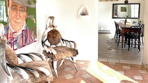 Een eetruimte met een grote tafel, meerdere stoelen, een wandlamp en een betegelde vloer.