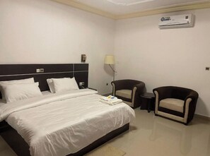 A hotel room with a bed, two armchairs, a bedside table, a lamp, and an air conditioning unit. - Beach Sand Hotel & Resort, Cotonou Standard King Room 1 (Cotonou)