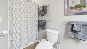 Une salle de bain avec un rideau de douche à motifs, des toilettes, un porte-serviettes avec des serviettes et un tableau encadré au mur.