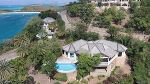 A large house with a swimming pool, surrounded by lush greenery and overlooking a coastal area with boats. - Villa Tramonto. Great view, pool, exclusive area and beach at walking distance. (St. Johns)