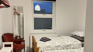 Une chambre à coucher comprenant un lit, une chaise, un bureau, une armoire et une fenêtre donnant sur le ciel.