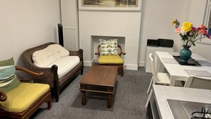 Un salon comprenant un canapé, un fauteuil et une table basse, un tableau au-dessus de la cheminée et un vase rempli de fleurs posé sur une table.