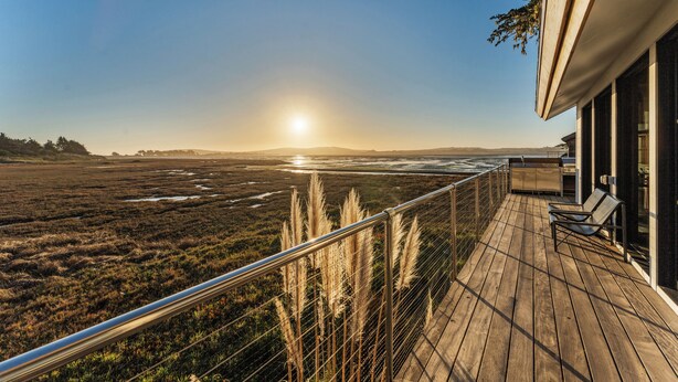 A wooden deck with a view of the ocean and distant hills.