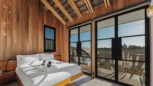A bedroom with a wooden ceiling, a large bed, a nightstand, a window, and a view of the outdoors.