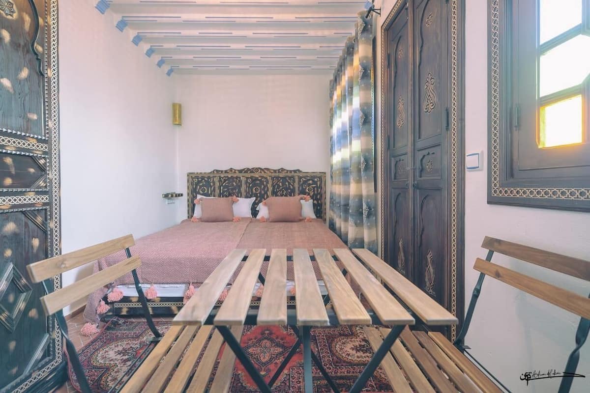 A room with a bed, wooden benches, and a patterned rug.
