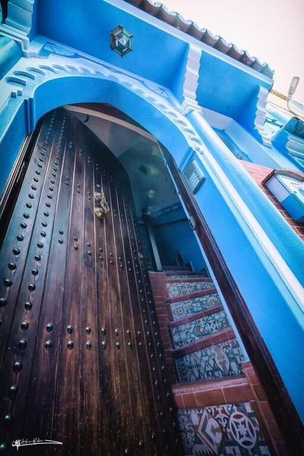 A wooden door with metal studs, leading to a staircase with patterned tiles. - Dar Rafik (Chefchaouen)