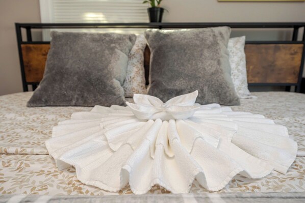 A neatly made bed with a decorative white towel arrangement in the center, a wooden headboard, and two gray pillows.