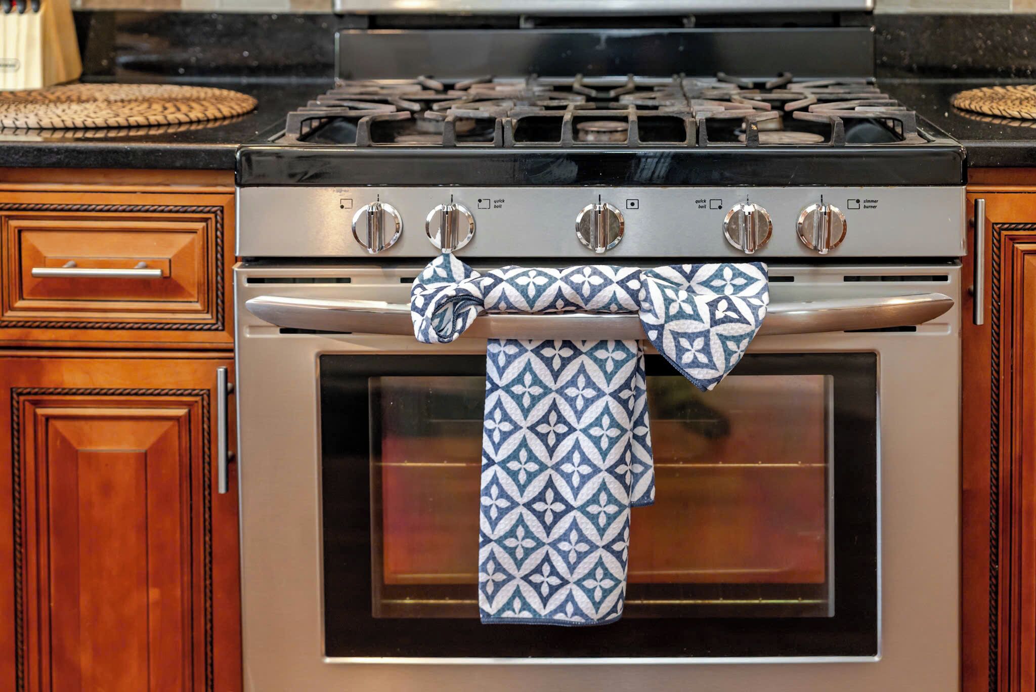 Una cocina con estufa y horno de acero inoxidable, armarios de madera y una toalla estampada colgada del mango del horno.