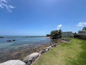 Un hôtel situé sur la côte, offrant une vue dégagée sur l’océan, avec un rivage rocheux et une zone herbeuse, un bâtiment se dressant à l’arrière-plan.