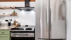 A kitchen with a stainless steel refrigerator, a stove, and a microwave. There are wooden shelves above the stove holding kitchen items. - Aspen Glow Cabin - a charming 2-bedroom cabin with mountain views & wood stove (Bailey)
