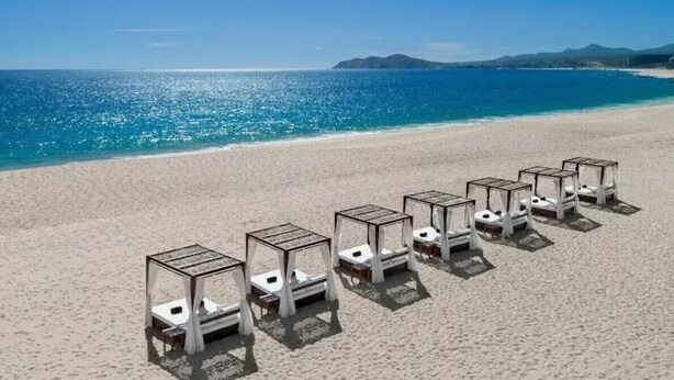 Une plage avec des chaises longues blanches disposées en rangées, face à l’océan.