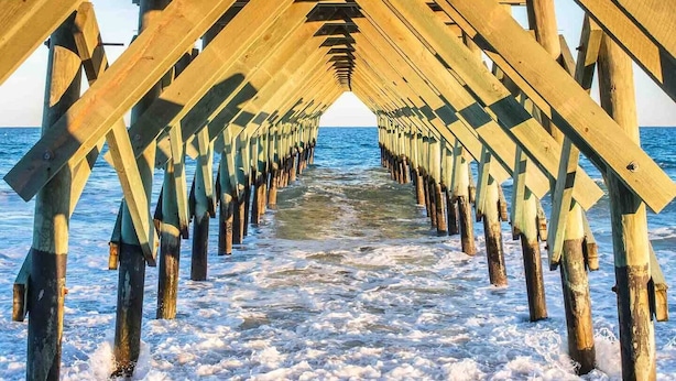 Eine hölzerne Mole, die sich ins Meer erstreckt, während Wellen an ihrem Fuße brechen.