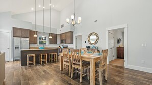 A spacious kitchen with wooden cabinets, a central island, and a dining area with wooden chairs and a table. - 4BR All Ensuite Baths + Bonus Living Area + Hot Tub + Pet-Friendly + Corolla Lt (Corolla)