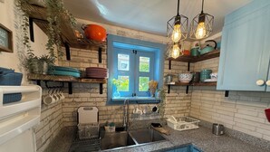 A kitchen with blue cabinets, a window with a view, hanging plants, and a sink. - Cozy 3-bedroom house in peaceful Juan Dolio with WiFi, AC (Juan Dolio)