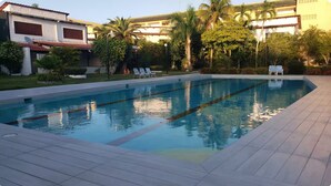 A rectangular swimming pool with clear water, surrounded by a tiled deck. There are lounge chairs and a small table in the pool area. - Cozy 3-bedroom house in peaceful Juan Dolio with WiFi, AC (Juan Dolio)