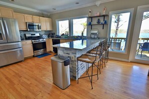 A modern kitchen with stainless steel appliances, a large island with bar stools, and a view of the outdoors.