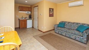 A compact living space with a kitchenette, a sofa with patterned upholstery, and a dining table with chairs.