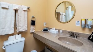 A bathroom with a sink, mirror, towels, toiletries, and a toilet.